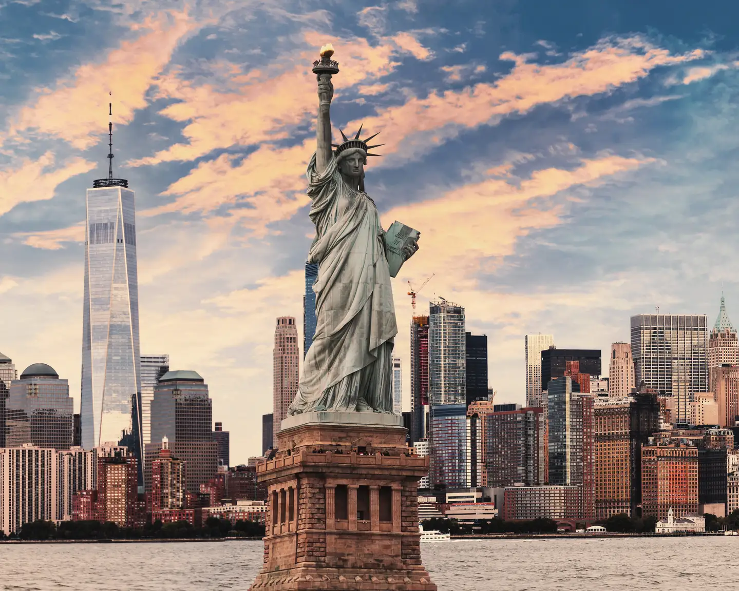 La estatua de la Libertad con el horizonte de Nueva York al fondo bajo un colorido cielo vespertino.