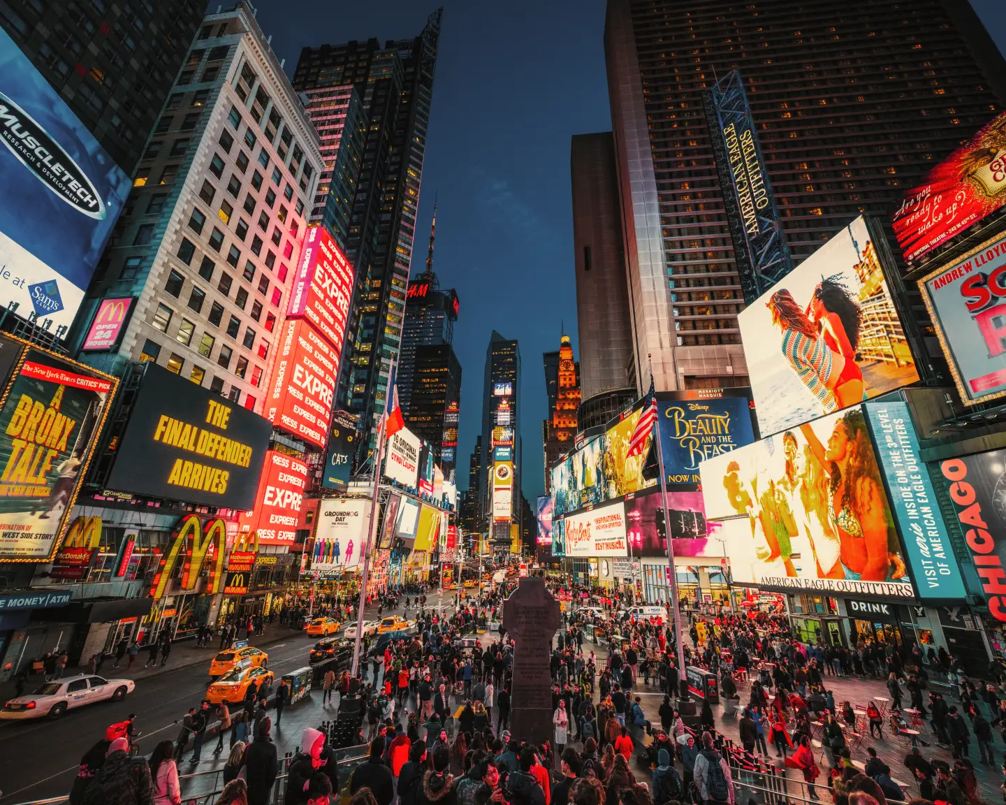 Der Broadway in New York bei Nacht mit erleuchteten Bildschirmen und Menschen im Vordergrund.