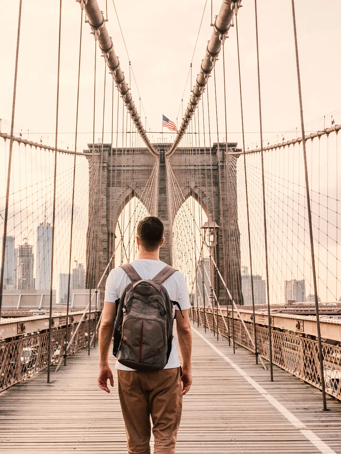 Vista trasera de un hombre con una mochila cruzando el puente de Brooklyn hacia Nueva York.