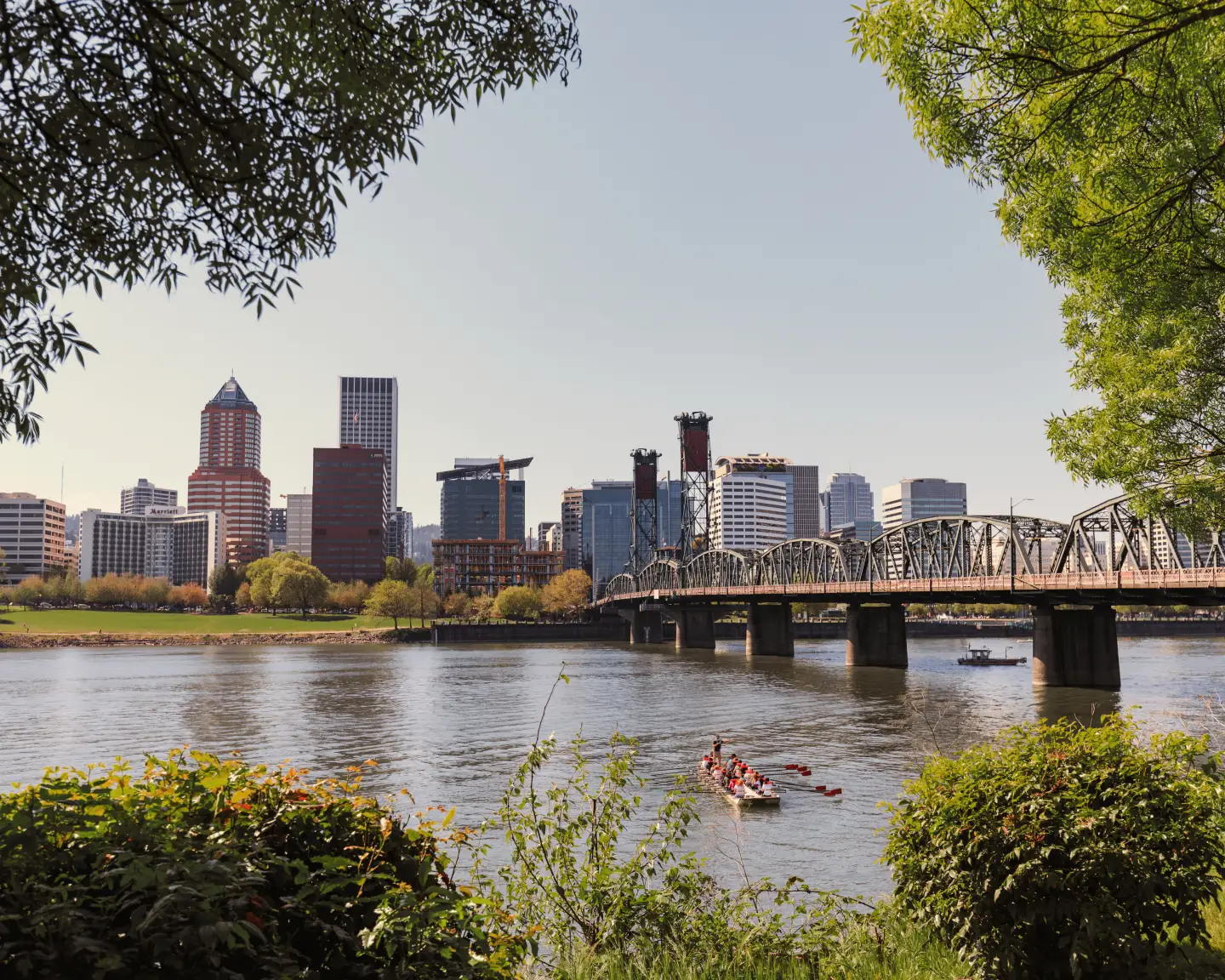 Vue de la silhouette urbaine de Portland, Oregon, avec un pont sur la rivière Willamette et des kayakistes dans l'eau, encadrée par des arbres.