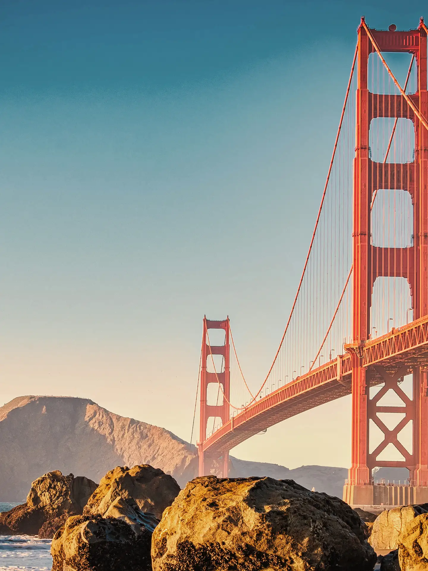 Puente Golden Gate en San Francisco, con un cielo azul claro y rocas en primer plano.