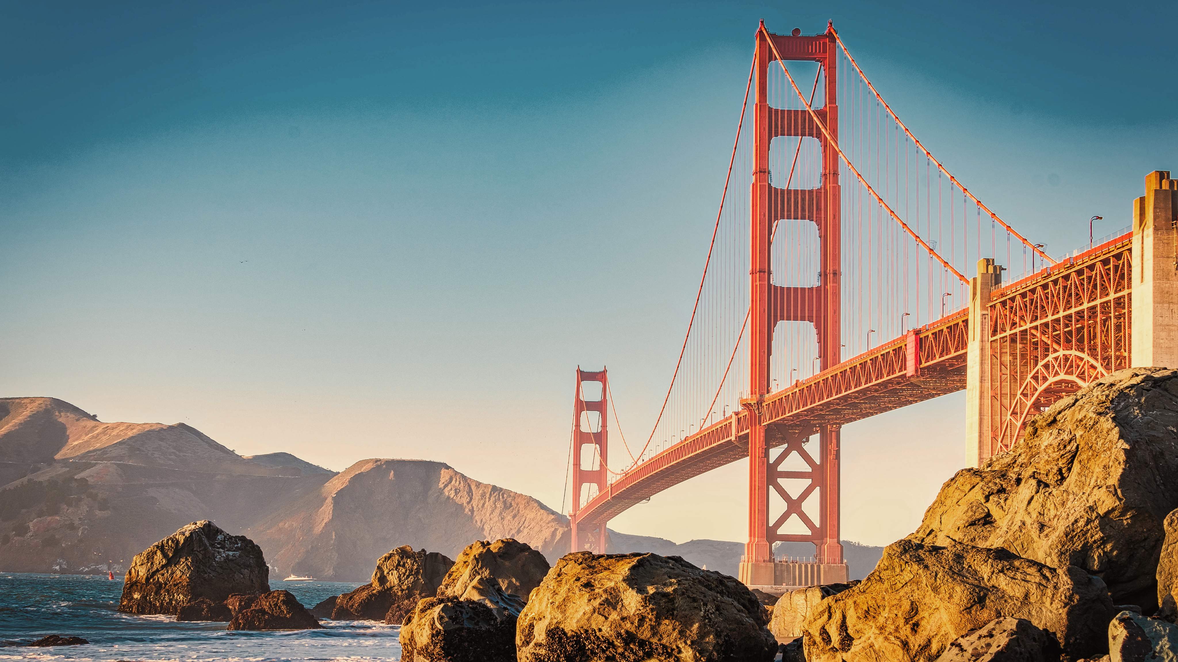 A Golden Gate híd San Franciscóban, tiszta kék égbolt alatt és sziklákkal az előtérben.