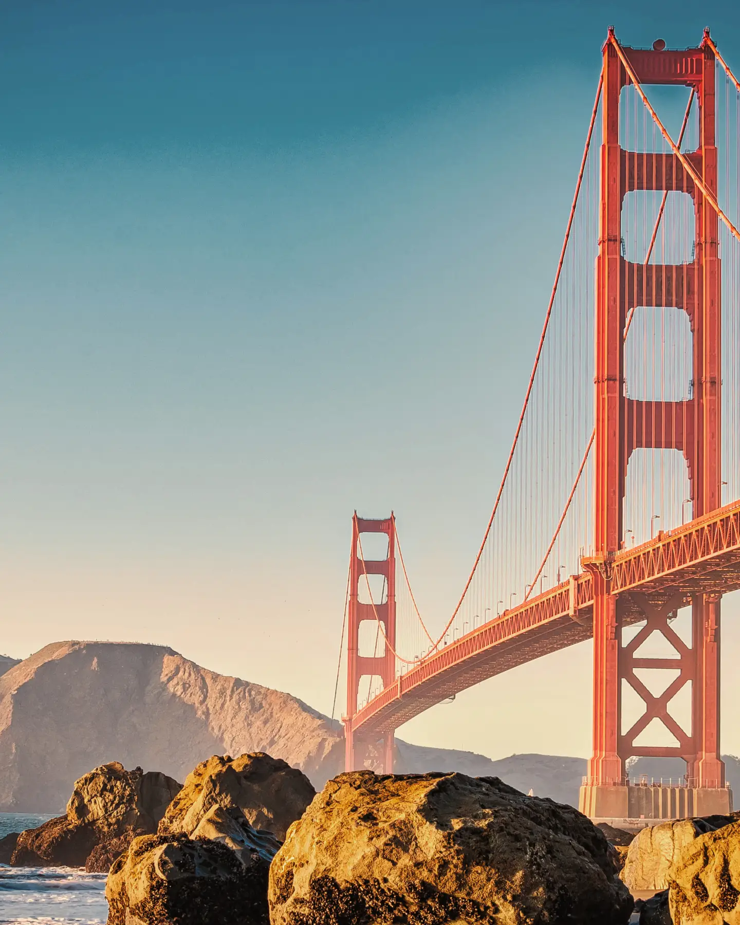 A Golden Gate híd San Franciscóban, tiszta kék égbolt alatt és sziklákkal az előtérben.