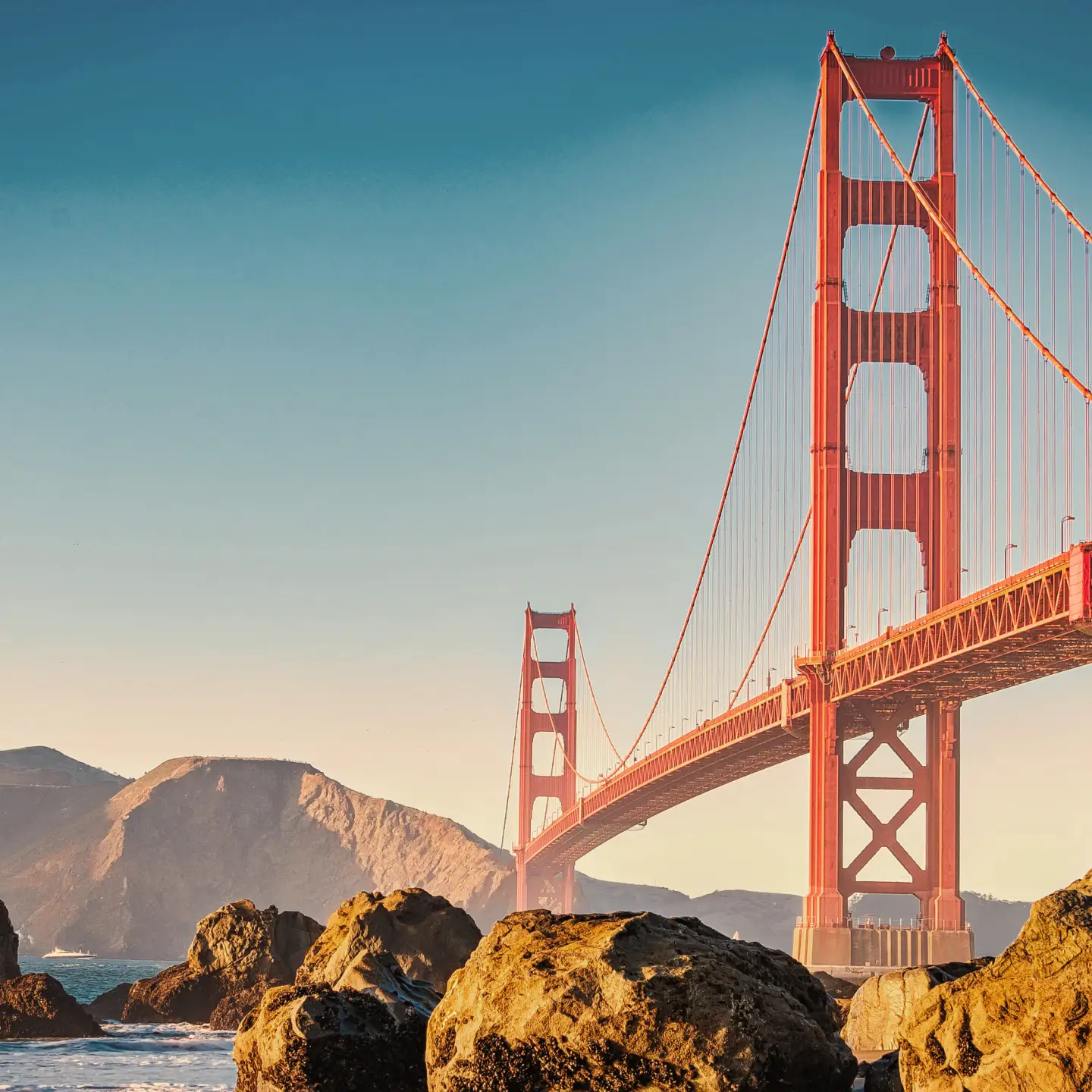 A Golden Gate híd San Franciscóban, tiszta kék égbolt alatt és sziklákkal az előtérben.