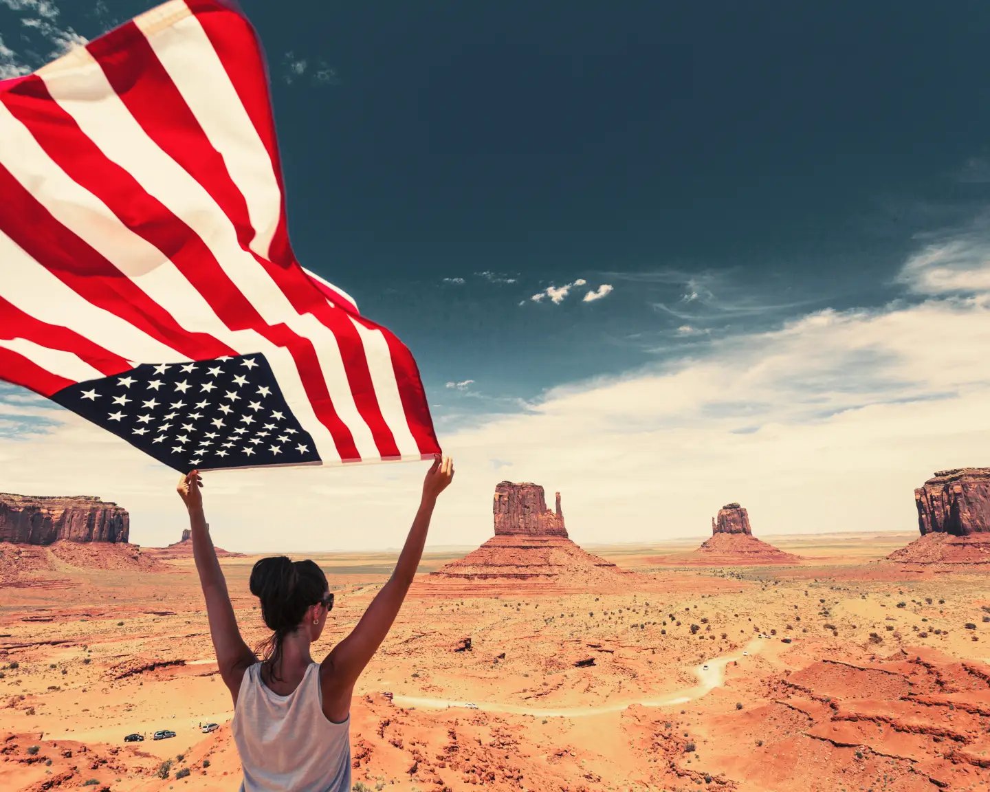 Egy nő amerikai zászlót tart a magasba a Monument Valleyben, a hatalmas kék ég alatt, ikonikus sziklaalakzatok között.