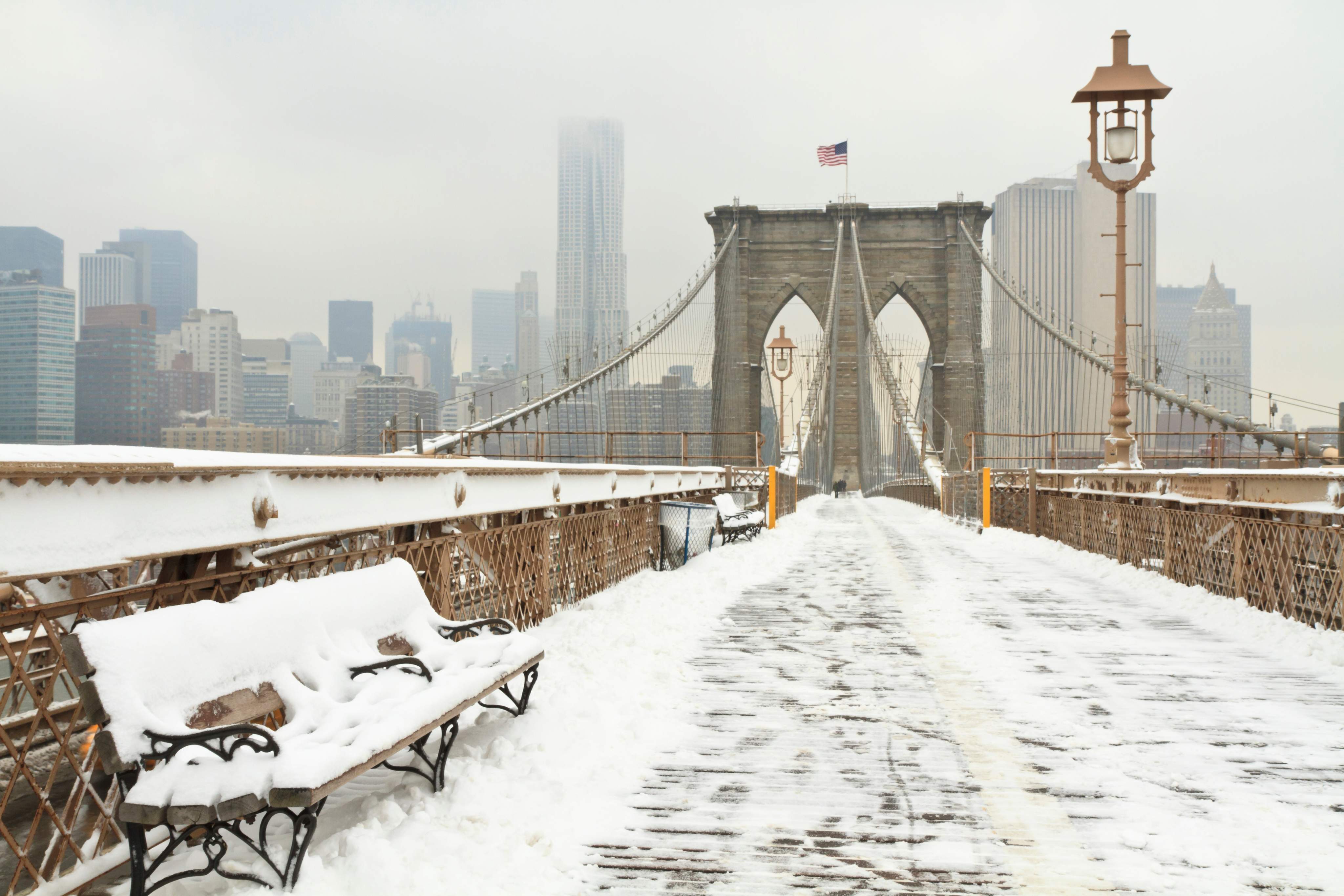 Ein horizontales Foto einer verschneiten Bank auf der Brooklyn Bridge während eines Schneesturms