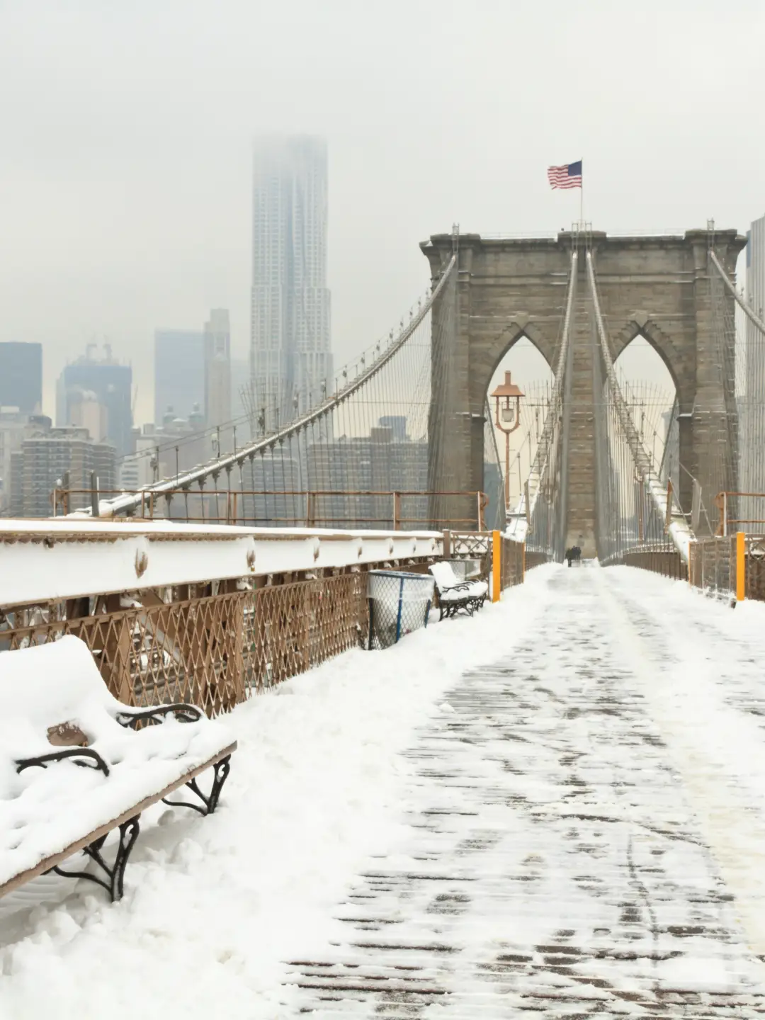 Ein horizontales Foto einer verschneiten Bank auf der Brooklyn Bridge während eines Schneesturms