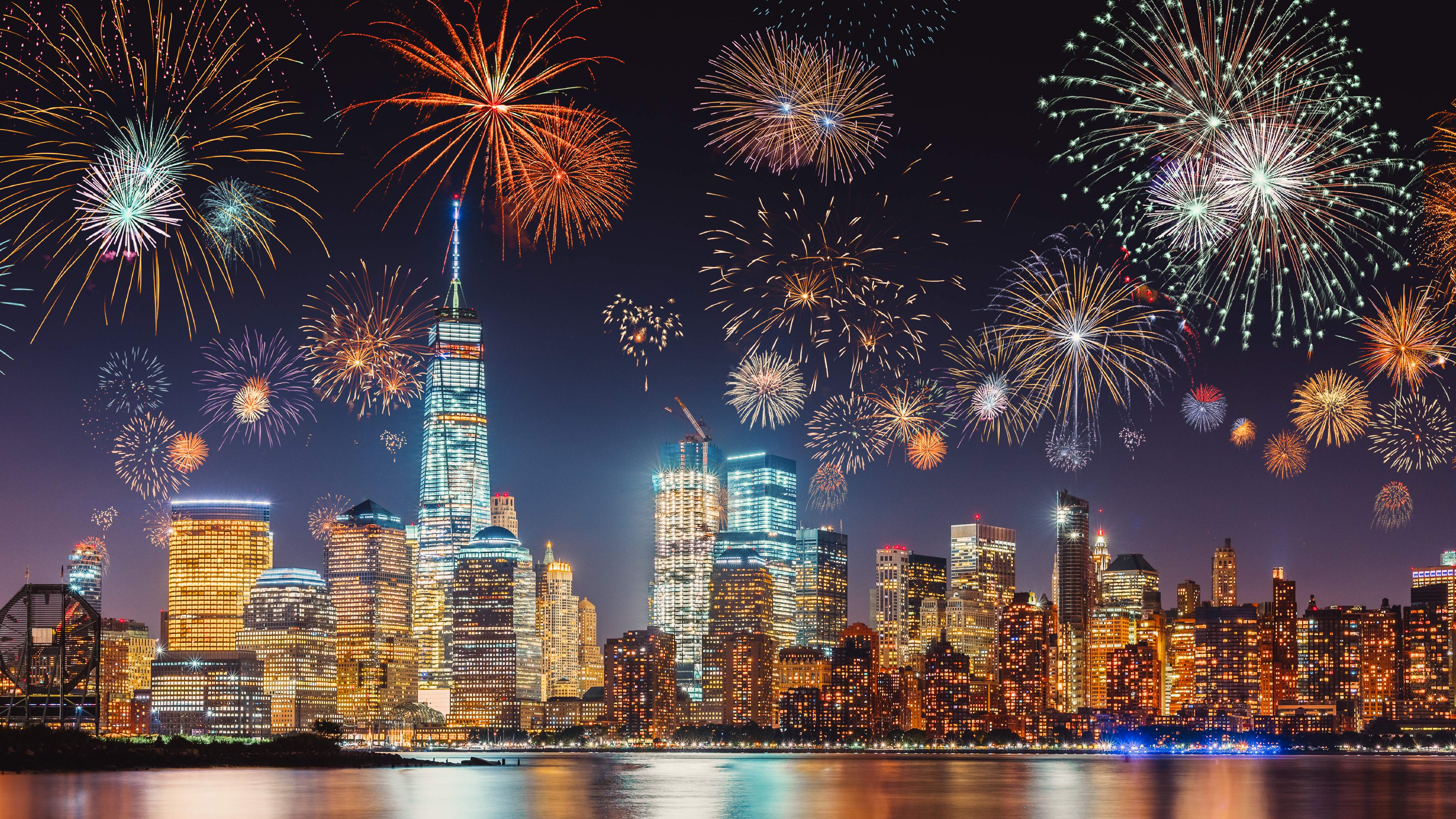 Réveillon du Nouvel An avec des feux d'artifice colorés au-dessus de la silhouette de New York, capturés en longue exposition avec un ciel bleu-violet foncé, une lueur orange des lumières de la ville et des reflets dans le fleuve