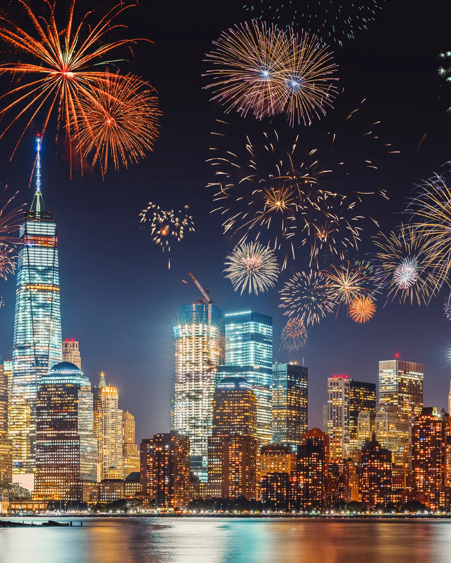 Réveillon du Nouvel An avec des feux d'artifice colorés au-dessus de la silhouette de New York, capturés en longue exposition avec un ciel bleu-violet foncé, une lueur orange des lumières de la ville et des reflets dans le fleuve