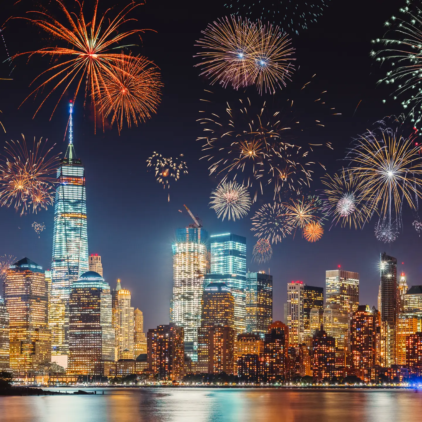 Réveillon du Nouvel An avec des feux d'artifice colorés au-dessus de la silhouette de New York, capturés en longue exposition avec un ciel bleu-violet foncé, une lueur orange des lumières de la ville et des reflets dans le fleuve