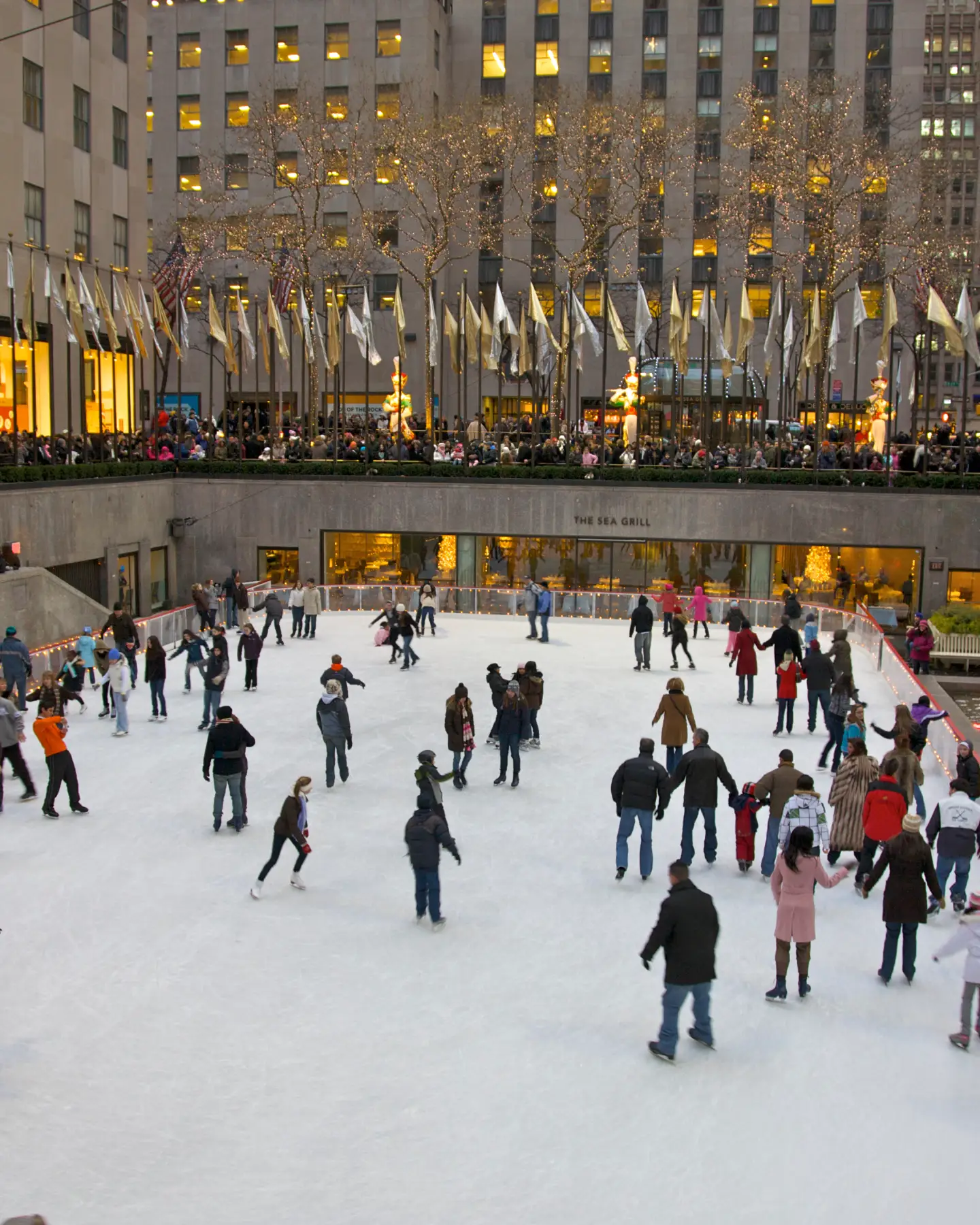 Menschen laufen Schlittschuh auf der berühmten Eislaufbahn am Rockefeller Center, umgeben von festlicher Beleuchtung und der winterlichen Atmosphäre in New York City.