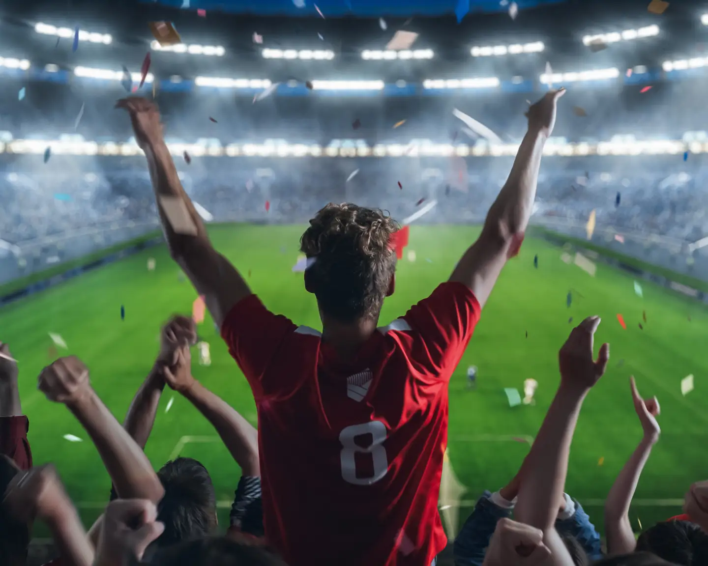 Un aficionado con una camiseta roja anima con los brazos en alto en un estadio abarrotado y lleno de confeti.