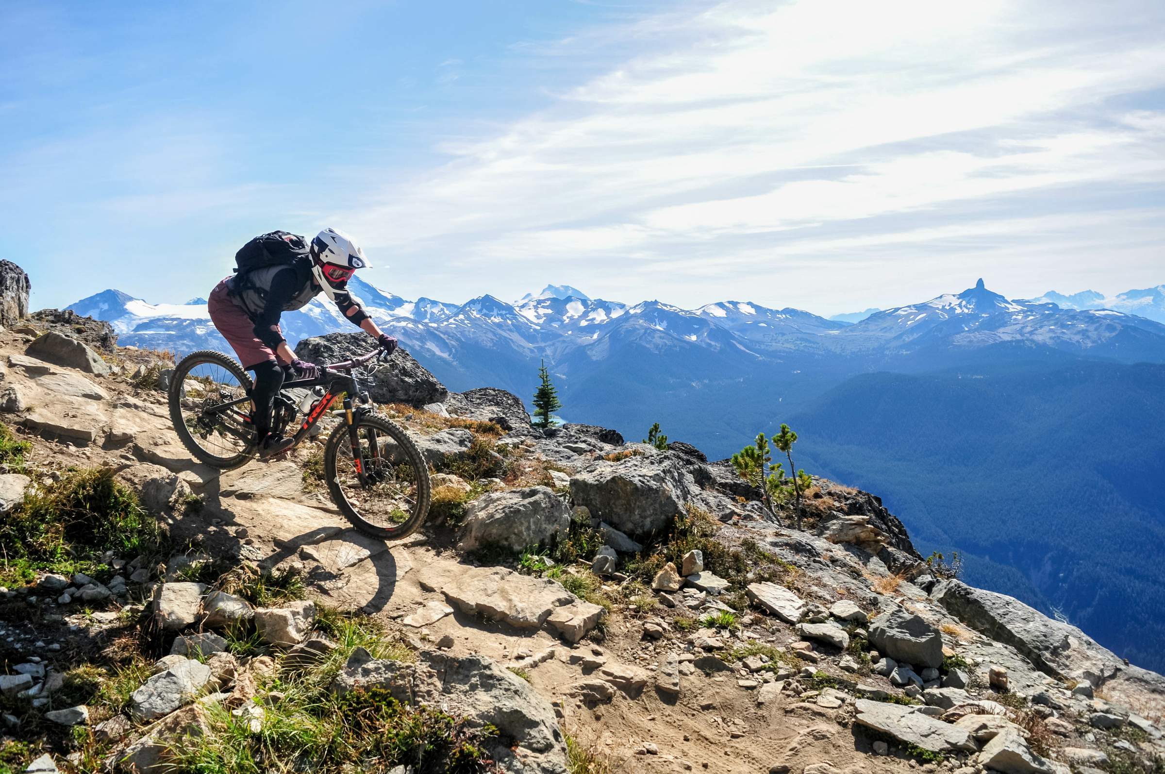 Ein Mountainbiker fährt auf einem felsigen Weg mit einem Panoramablick auf schneebedeckte Berge im Hintergrund.