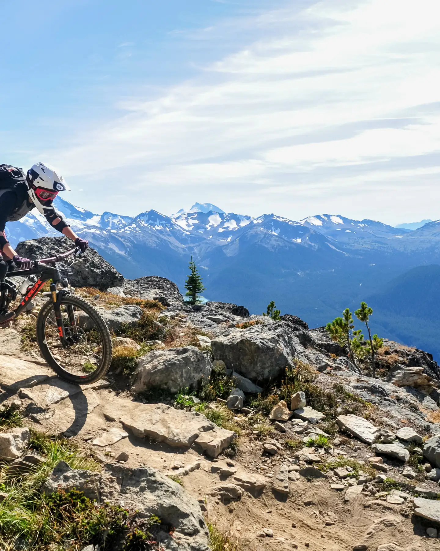 Ein Mountainbiker fährt auf einem felsigen Weg mit einem Panoramablick auf schneebedeckte Berge im Hintergrund.