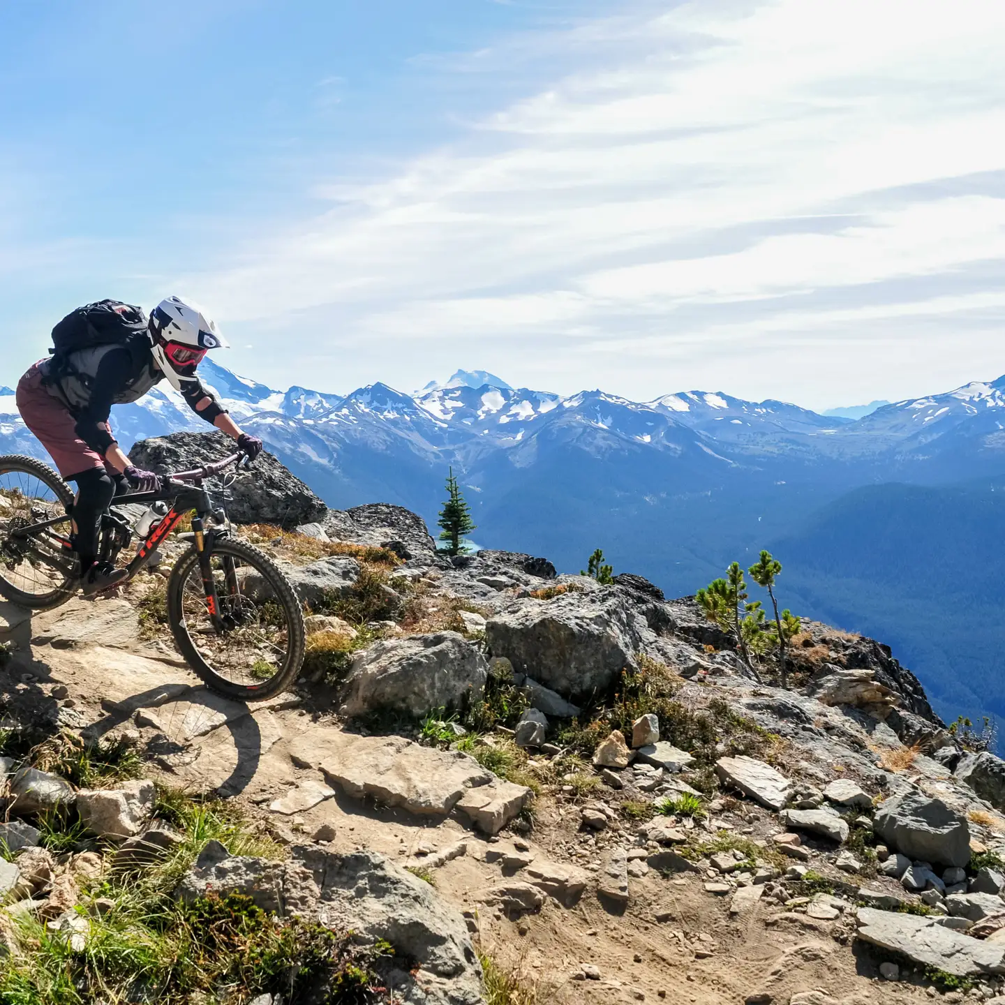 Ein Mountainbiker fährt auf einem felsigen Weg mit einem Panoramablick auf schneebedeckte Berge im Hintergrund.