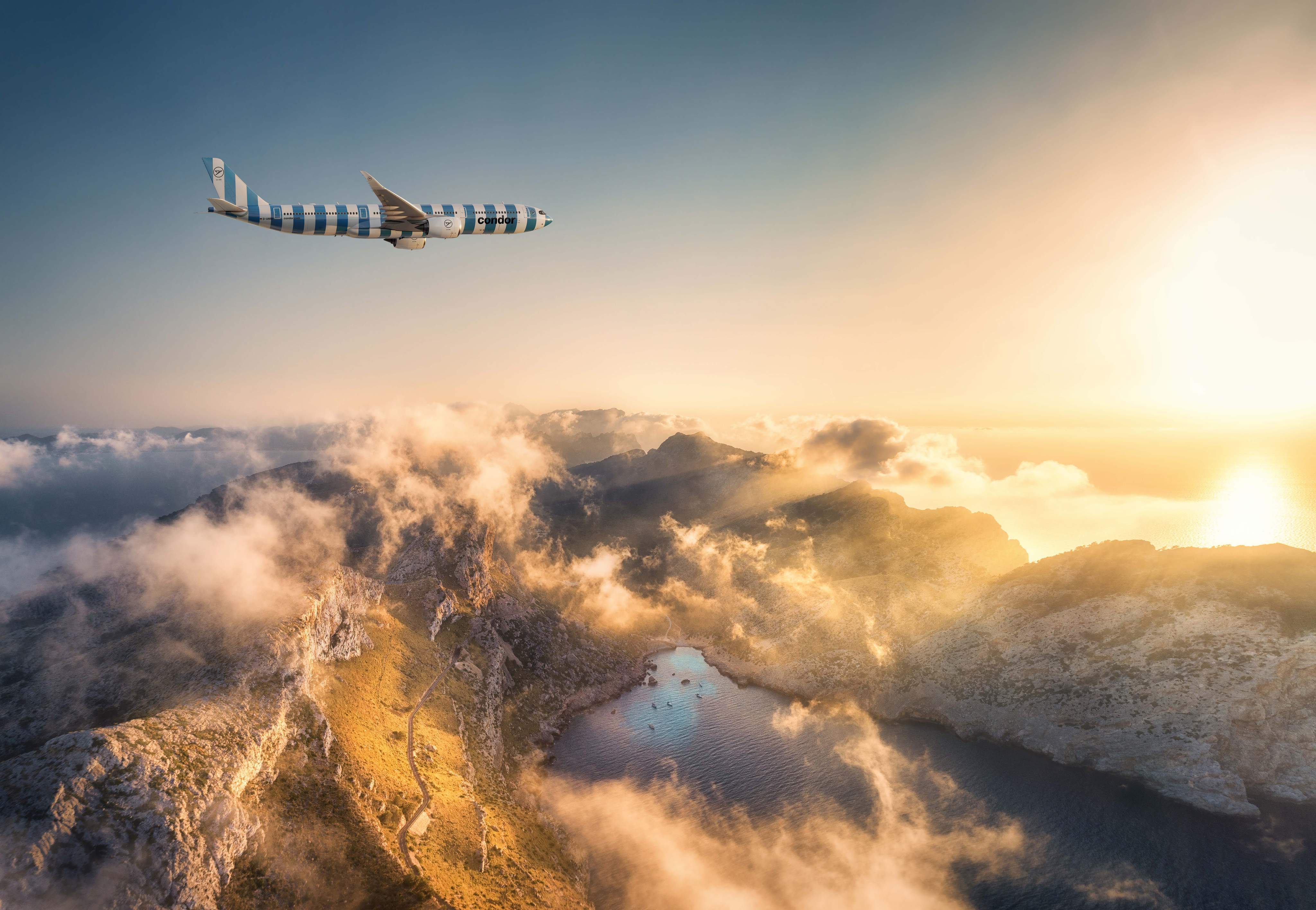 Airbus A330neo letící nad členitým pohořím, se sluncem, modrou oblohou a několika mraky v pozadí.