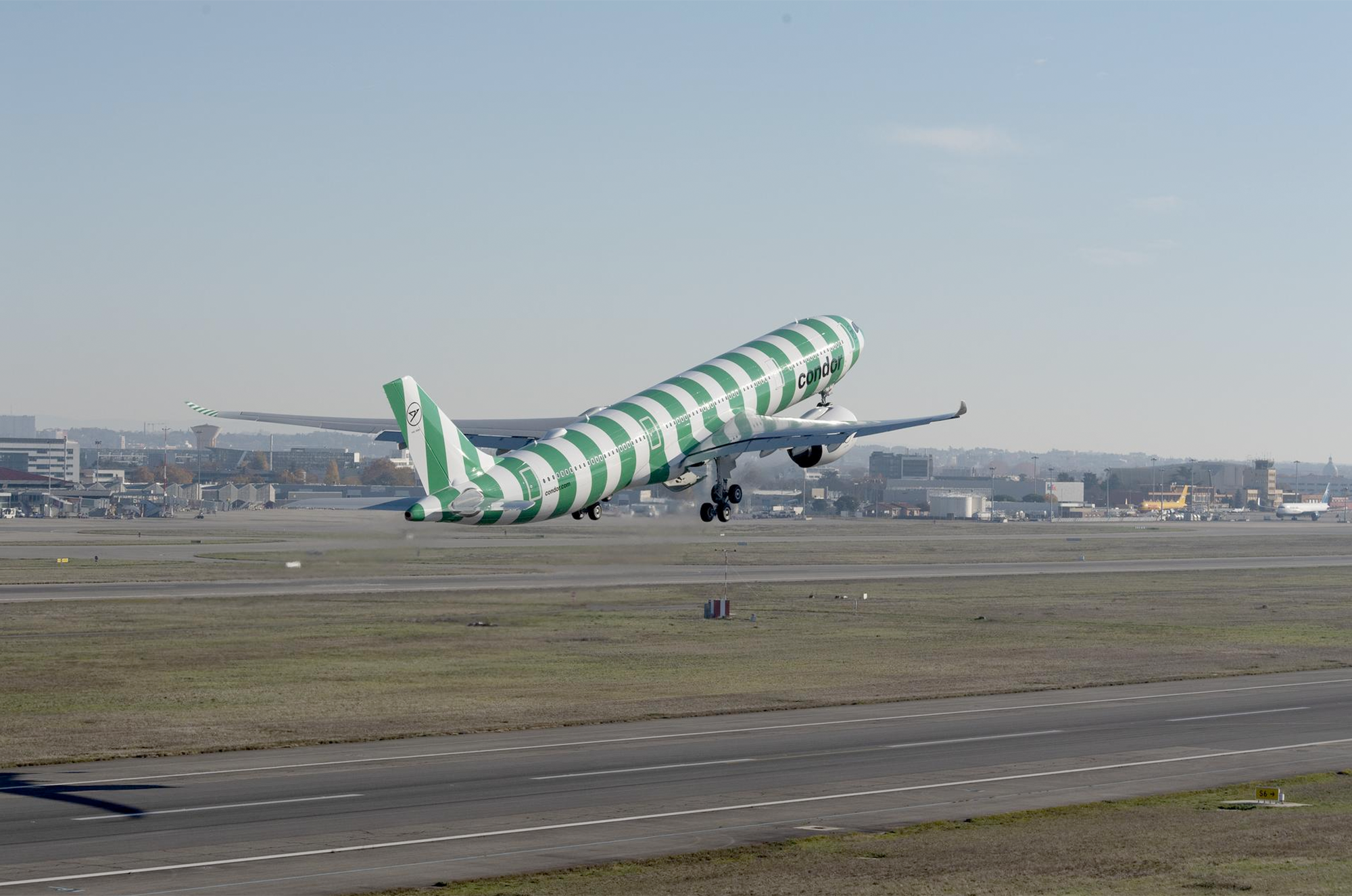 A Condor airplane with green and white stripes takes off from a runway.