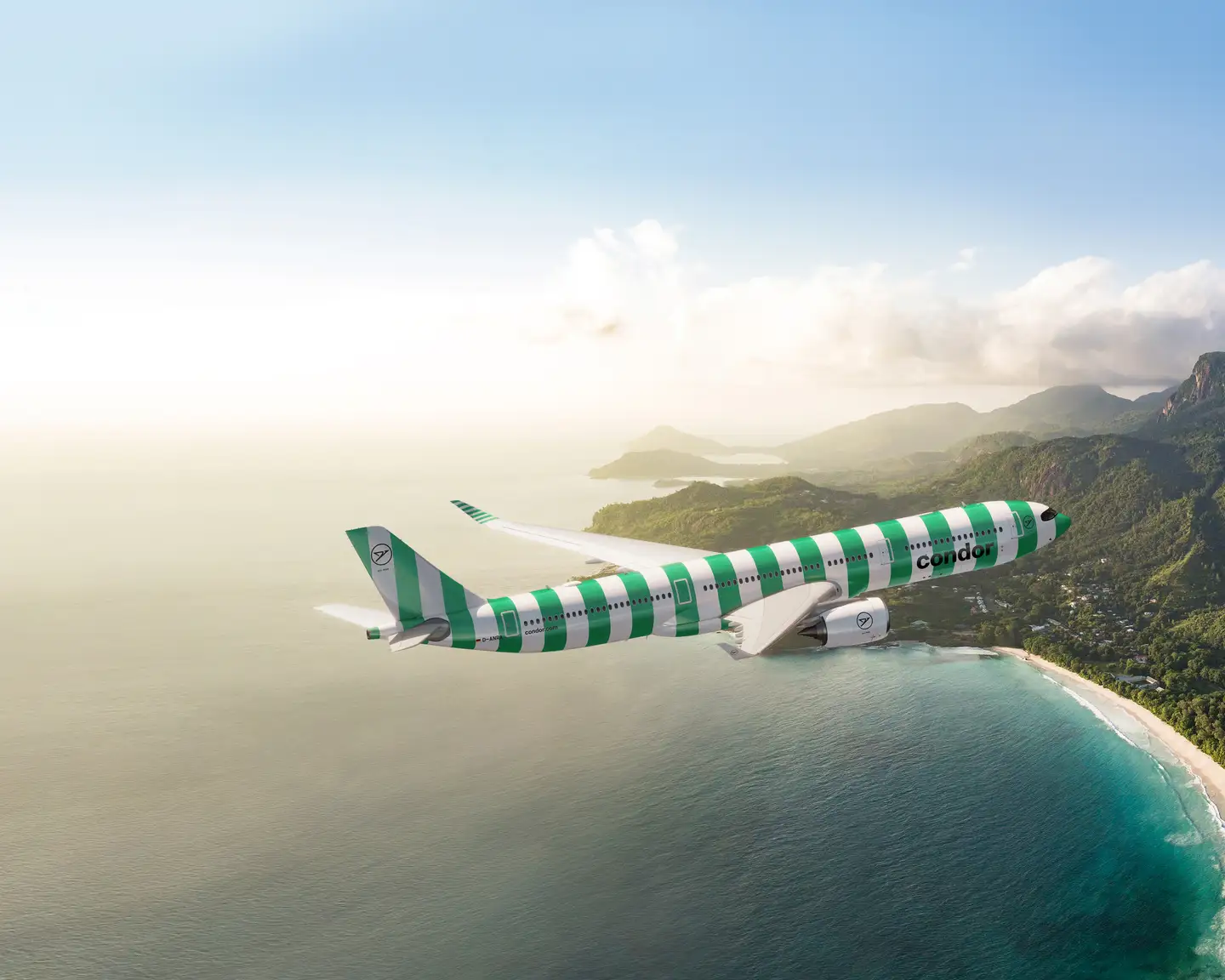 Vista de la impresionante playa de Grand Anse, la costa oeste y las colinas y montañas circundantes de la isla de Mahé, justo antes de la puesta del sol. Un Airbus 330neo de Condor, con rayas verdes y blancas, sobrevuela el cielo. 