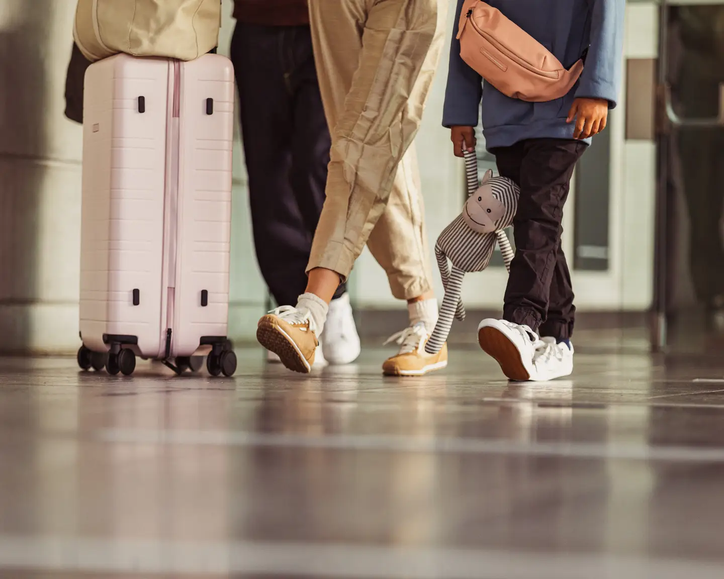 Familia caminando por el aeropuerto con maletas y el niño sostiene un juguete de peluche.