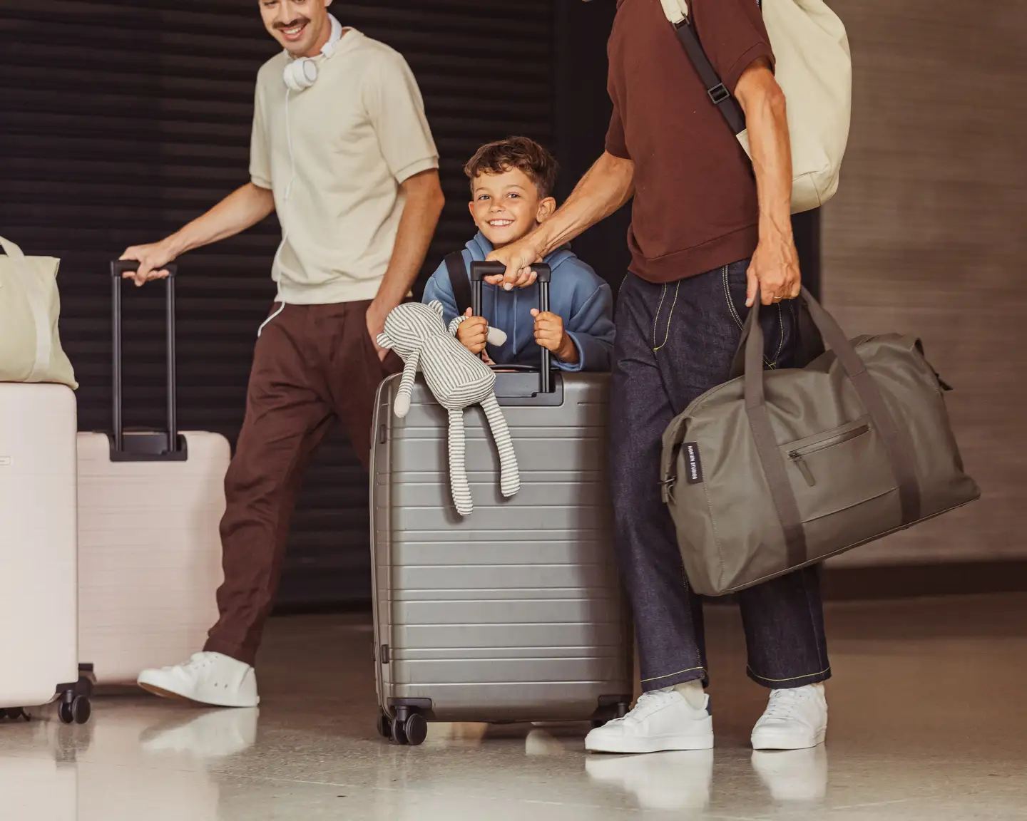 Niño sentado en una maleta, acompañado de dos adultos con más equipaje.