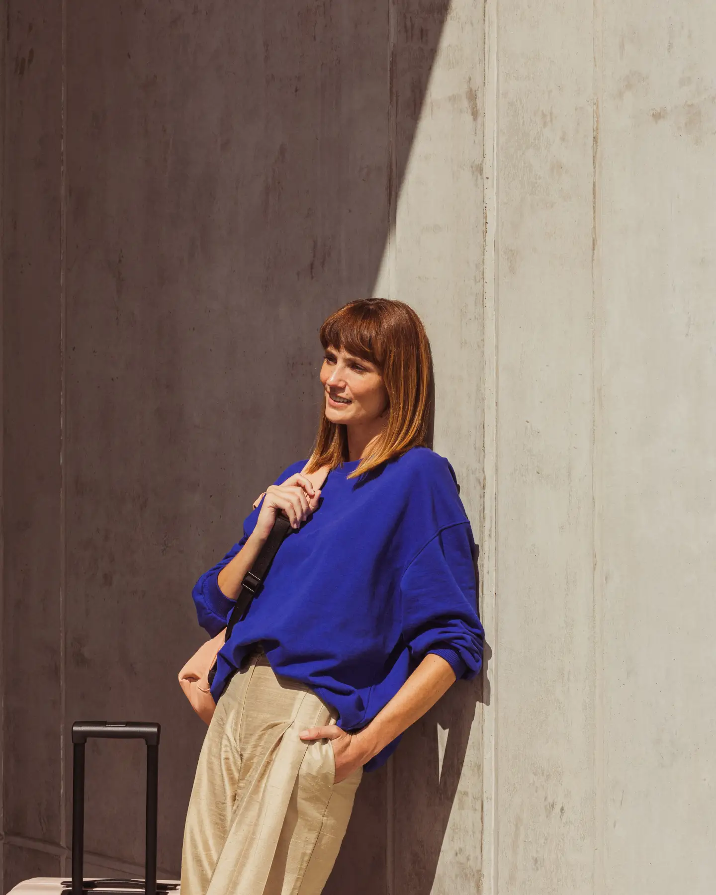 A woman leaning against the wall with her suitcase and waiting for an airport shuttle