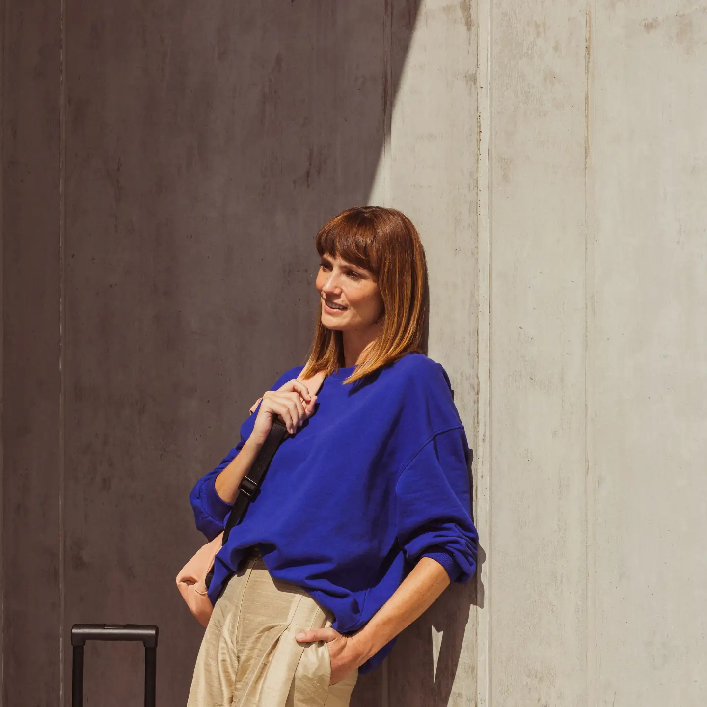 A woman leaning against the wall with her suitcase and waiting for an airport shuttle