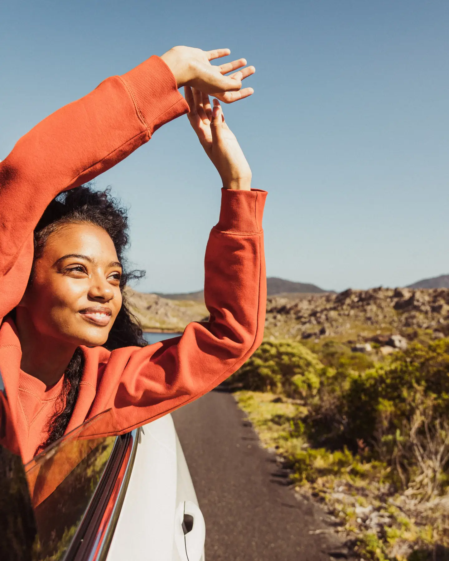 A woman extends her arms out of the open car window.