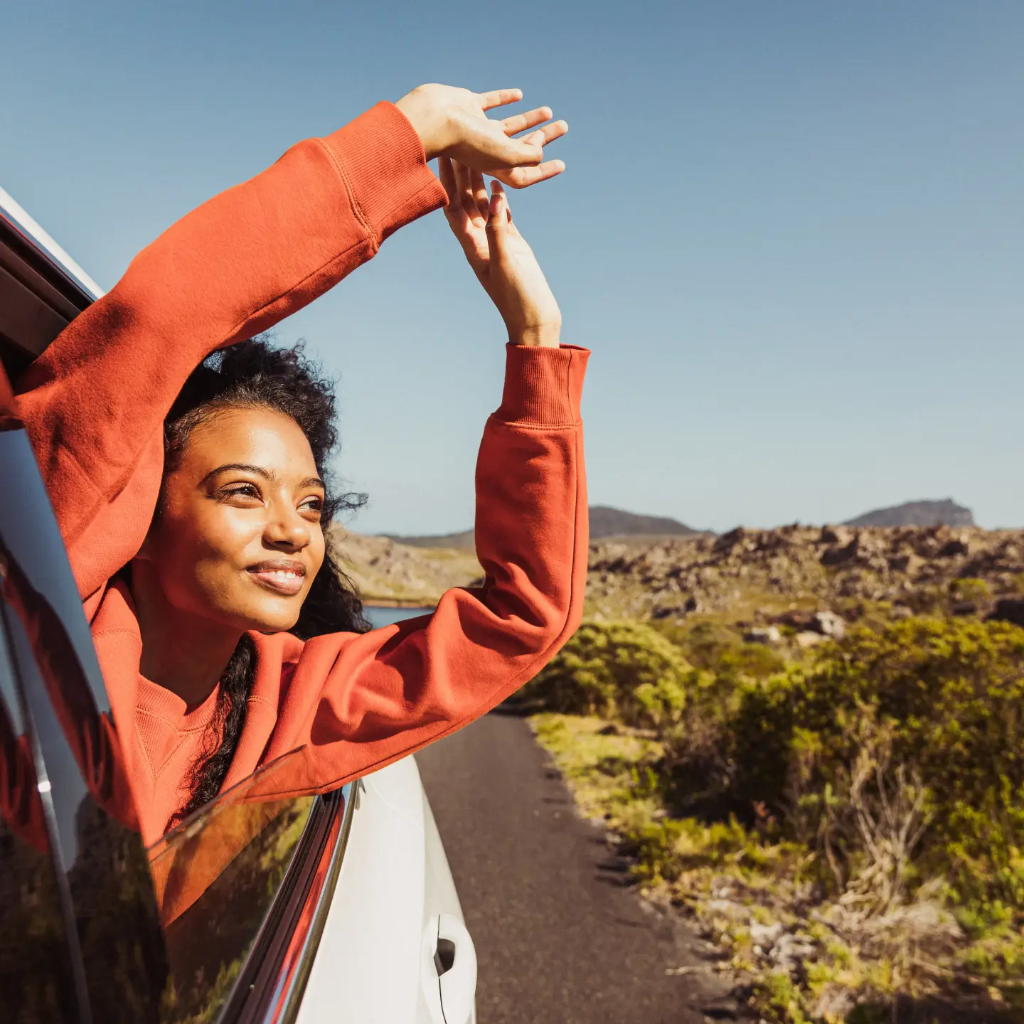 A woman extends her arms out of the open car window.