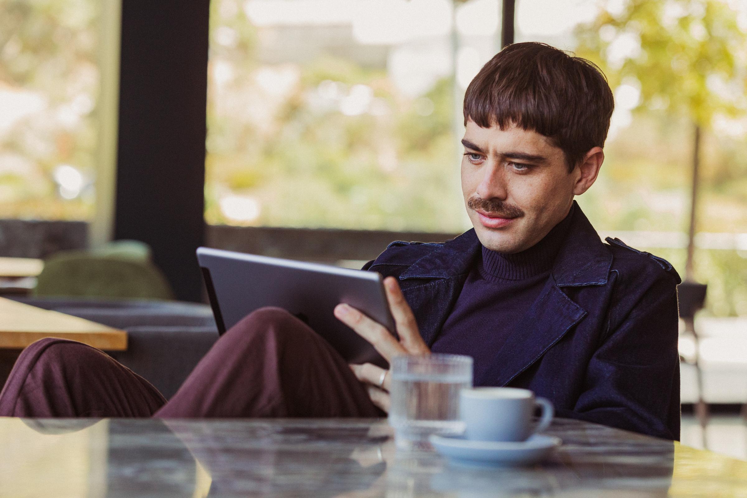 Un hombre está sentado a la mesa de una cafetería mirando su tableta.