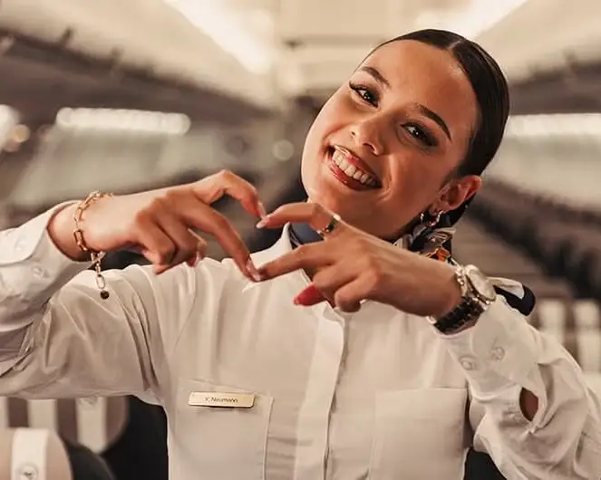 Smiling Condor flight attendant forms a heart with her hands in the aircraft cabin.