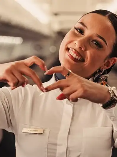 Smiling Condor flight attendant forms a heart with her hands in the aircraft cabin.
