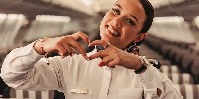 Smiling Condor flight attendant forms a heart with her hands in the aircraft cabin.