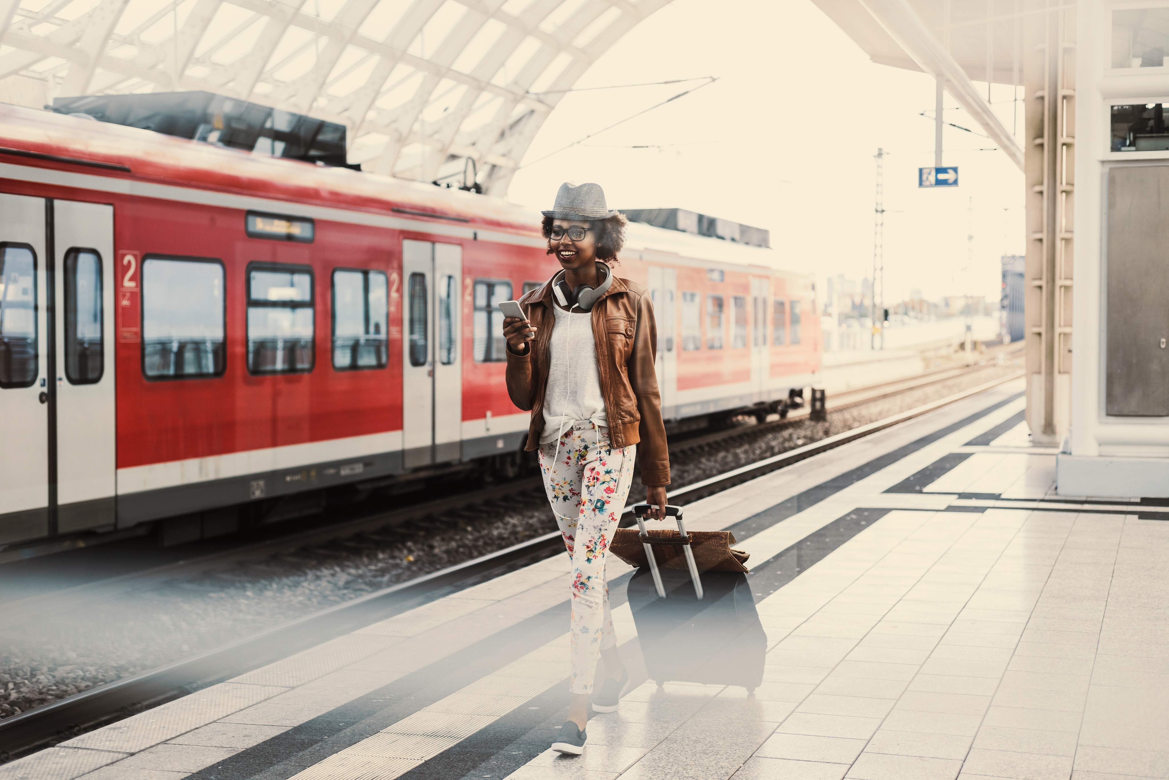 Mujer caminando por el andén con una maleta, con un tren rojo de Deutsche Bahn al fondo.