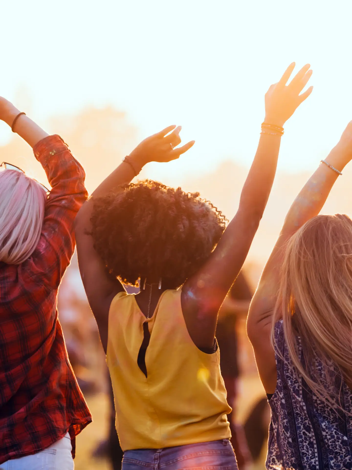 Trois amis profitent d'un festival en plein air et dansent les bras levés sous le soleil du soir.