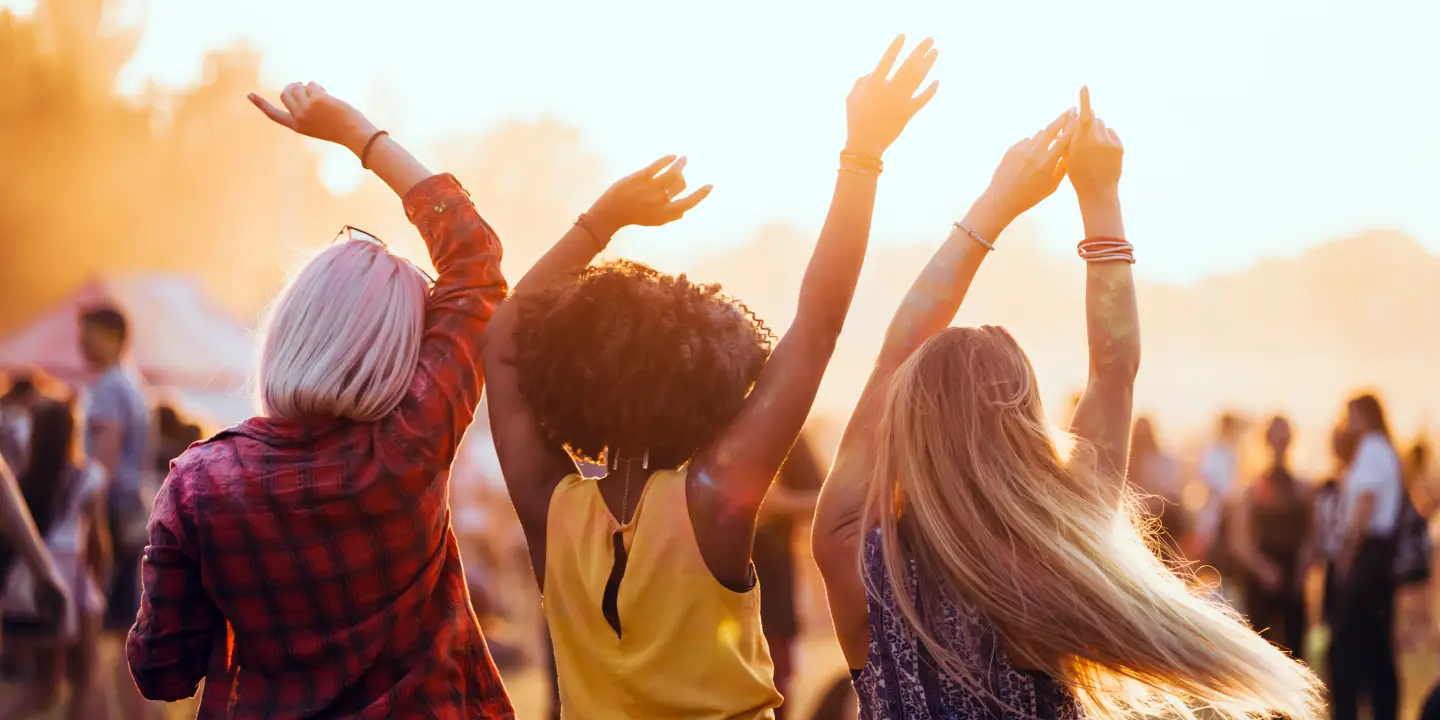 Trois amis profitent d'un festival en plein air et dansent les bras levés sous le soleil du soir.
