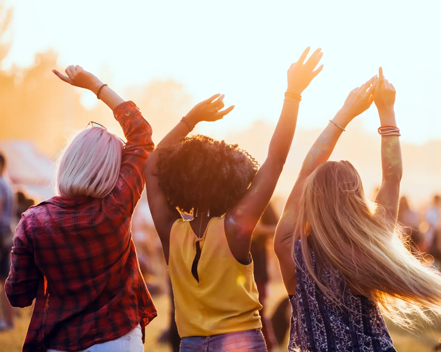 Drei Freunde genießen ein Open-Air-Festival und tanzen mit erhobenen Armen in der Abendsonne.