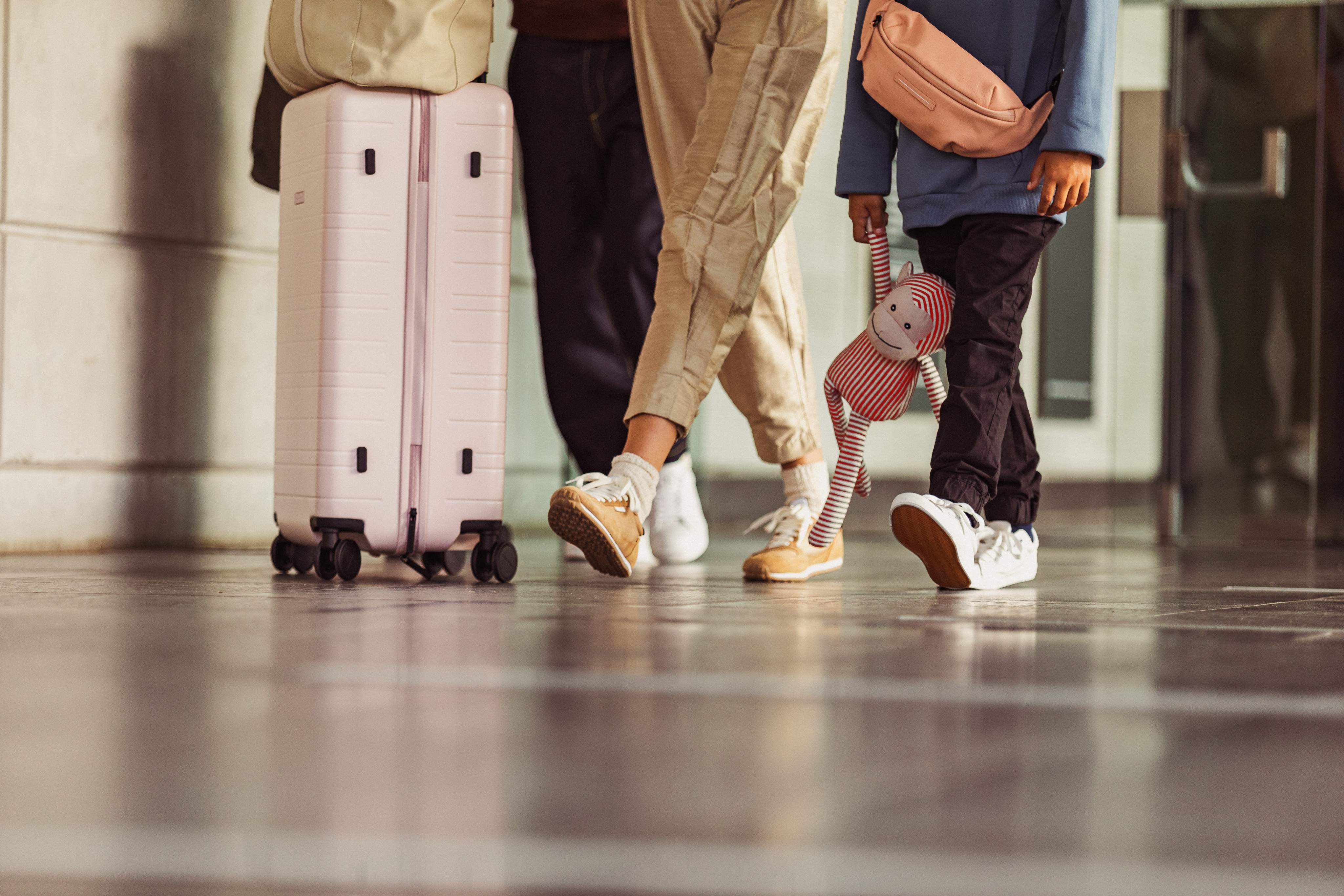 Een groep passagiers met hun bagage, waarbij alleen hun benen en koffers zichtbaar zijn, en een kind dat een knuffeldier vasthoudt