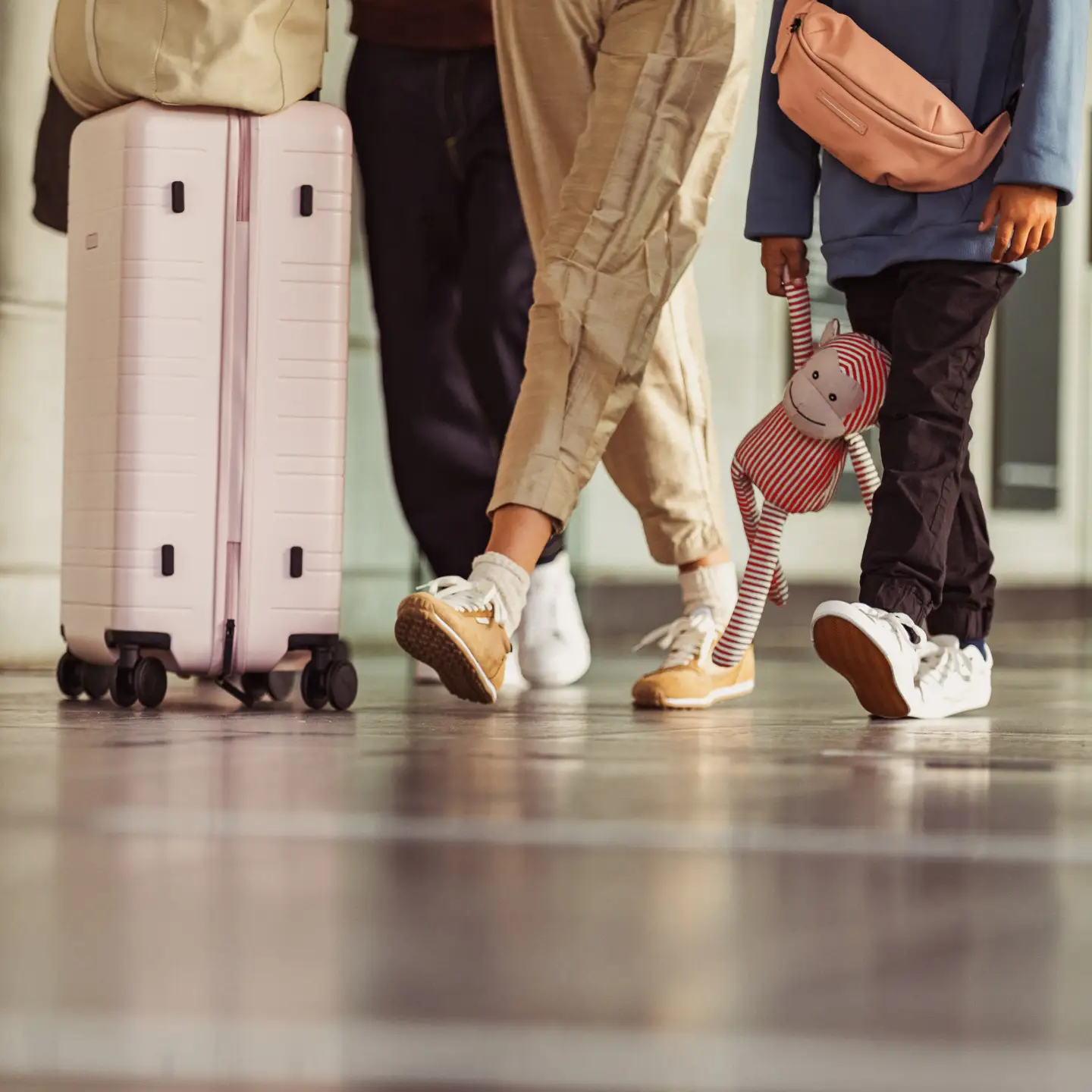 Een groep passagiers met hun bagage, waarbij alleen hun benen en koffers zichtbaar zijn, en een kind dat een knuffeldier vasthoudt