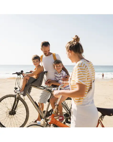 Familie mit zwei Kindern fährt im Urlaub gemeinsam mit Fahrrädern am Strand.