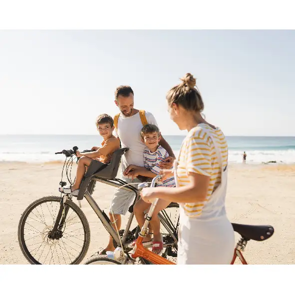 Familie mit zwei Kindern fährt im Urlaub gemeinsam mit Fahrrädern am Strand.