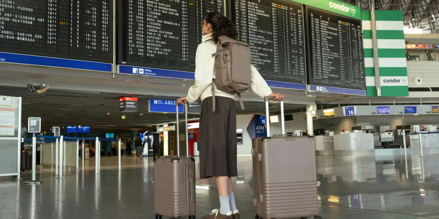 Frau steht mit Gepäck in der Terminal Eingangshalle an der Anzeigetafel.