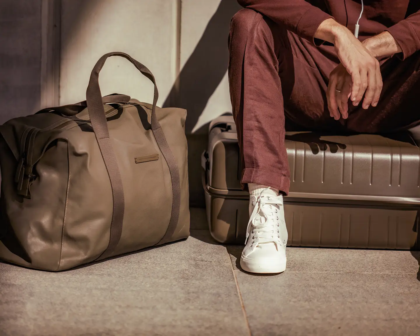 Una imagen recortada de un hombre sentado en su maleta, con su equipaje de mano a su lado.