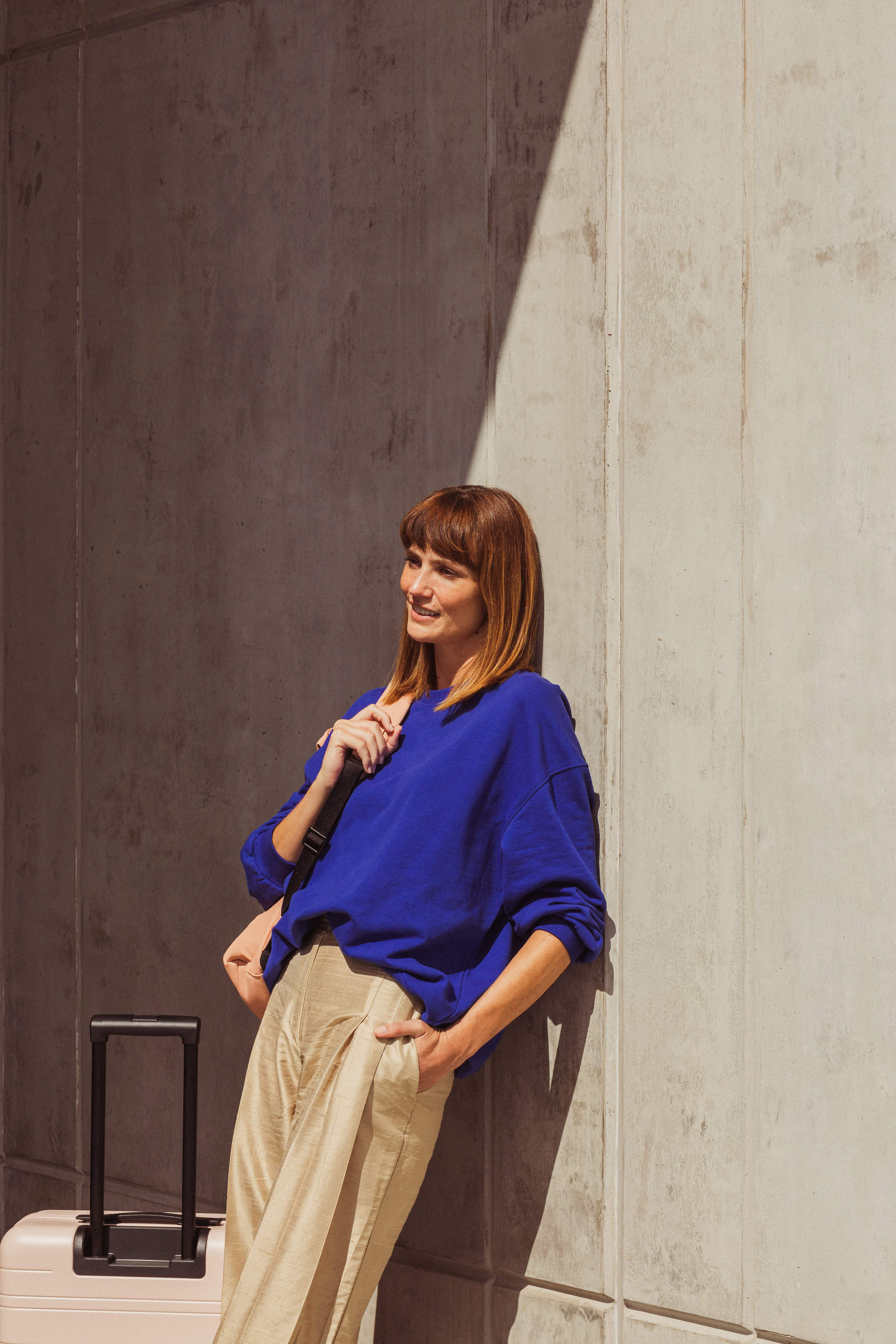 Een vrouw die met haar koffer tegen de muur leunt en wacht op een luchthavenshuttle