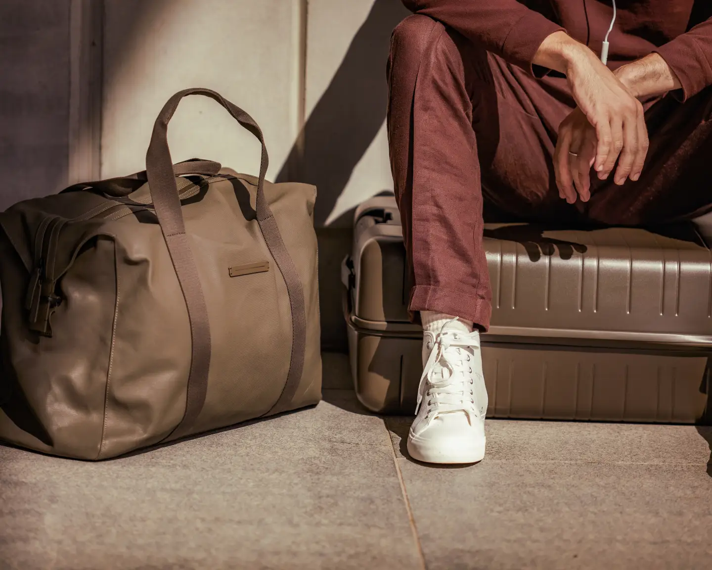 A cropped image of a man sitting on his suitcase, with his carry-on baggage beside him.