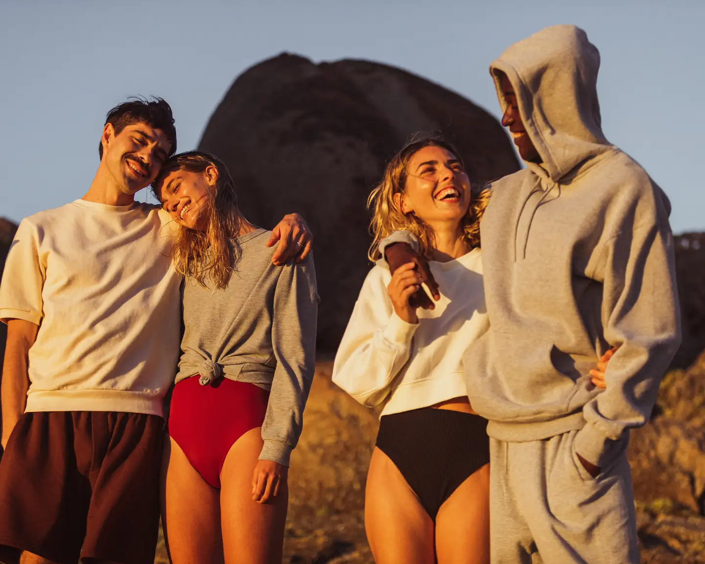 Un grupo de cuatro amigos está de pie en una playa al atardecer.