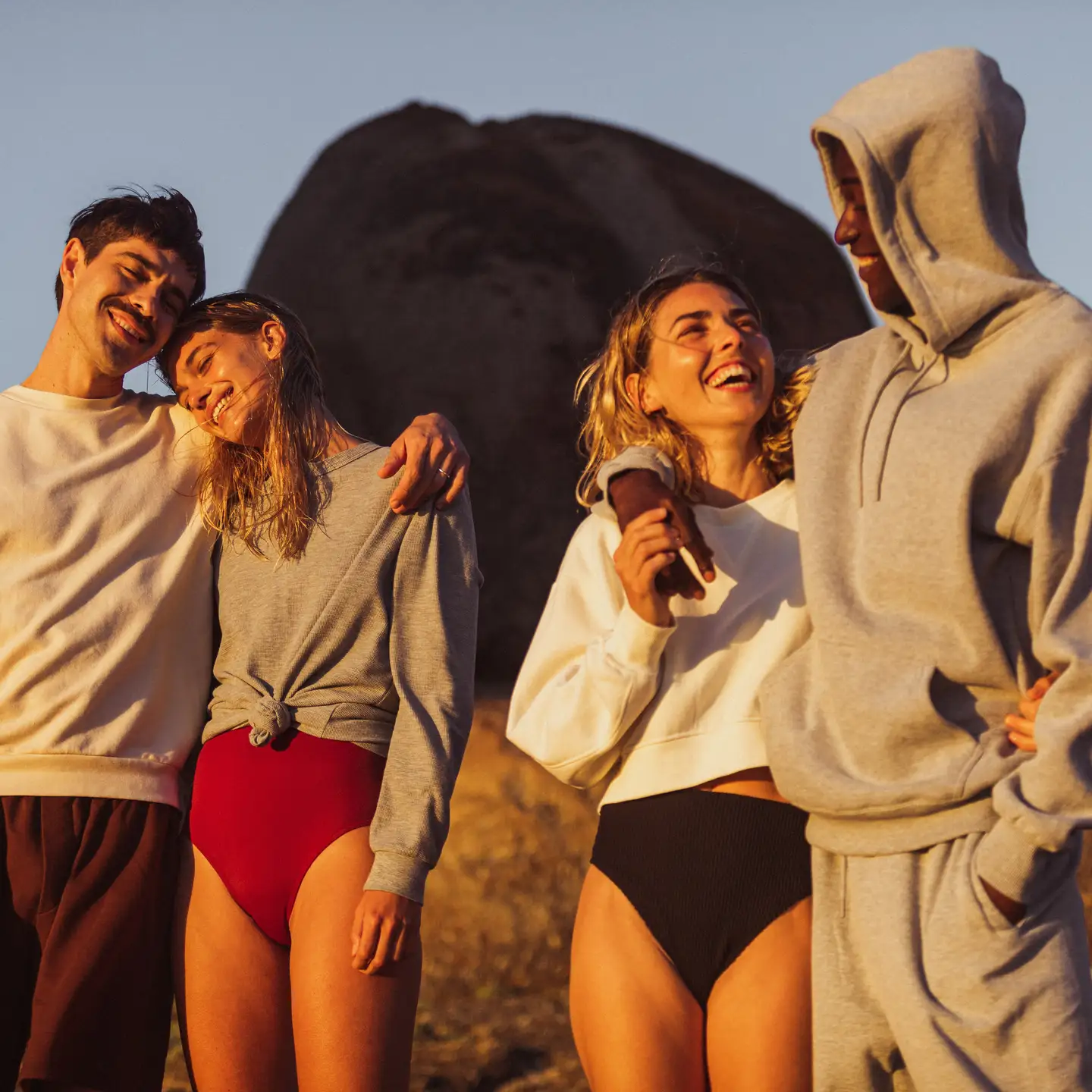 Un grupo de cuatro amigos está de pie en una playa al atardecer.