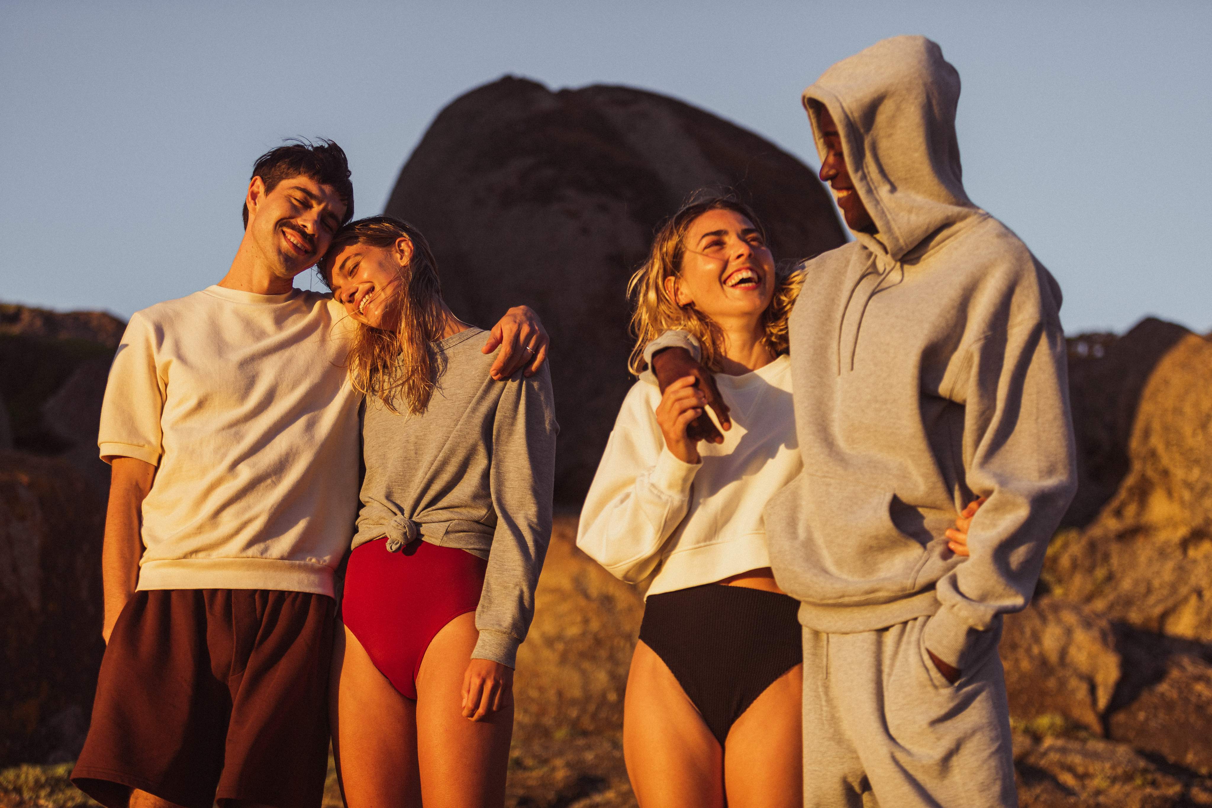 Un groupe de quatre amis se tient sur une plage au coucher du soleil.