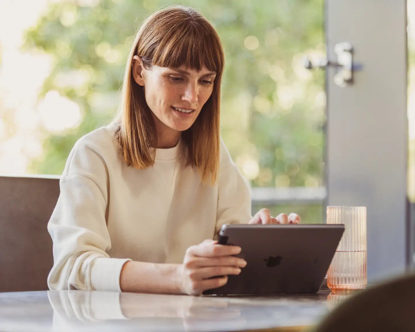 Een blonde vrouw gebruikt haar tablet om thuis online in te checken bij Condor.