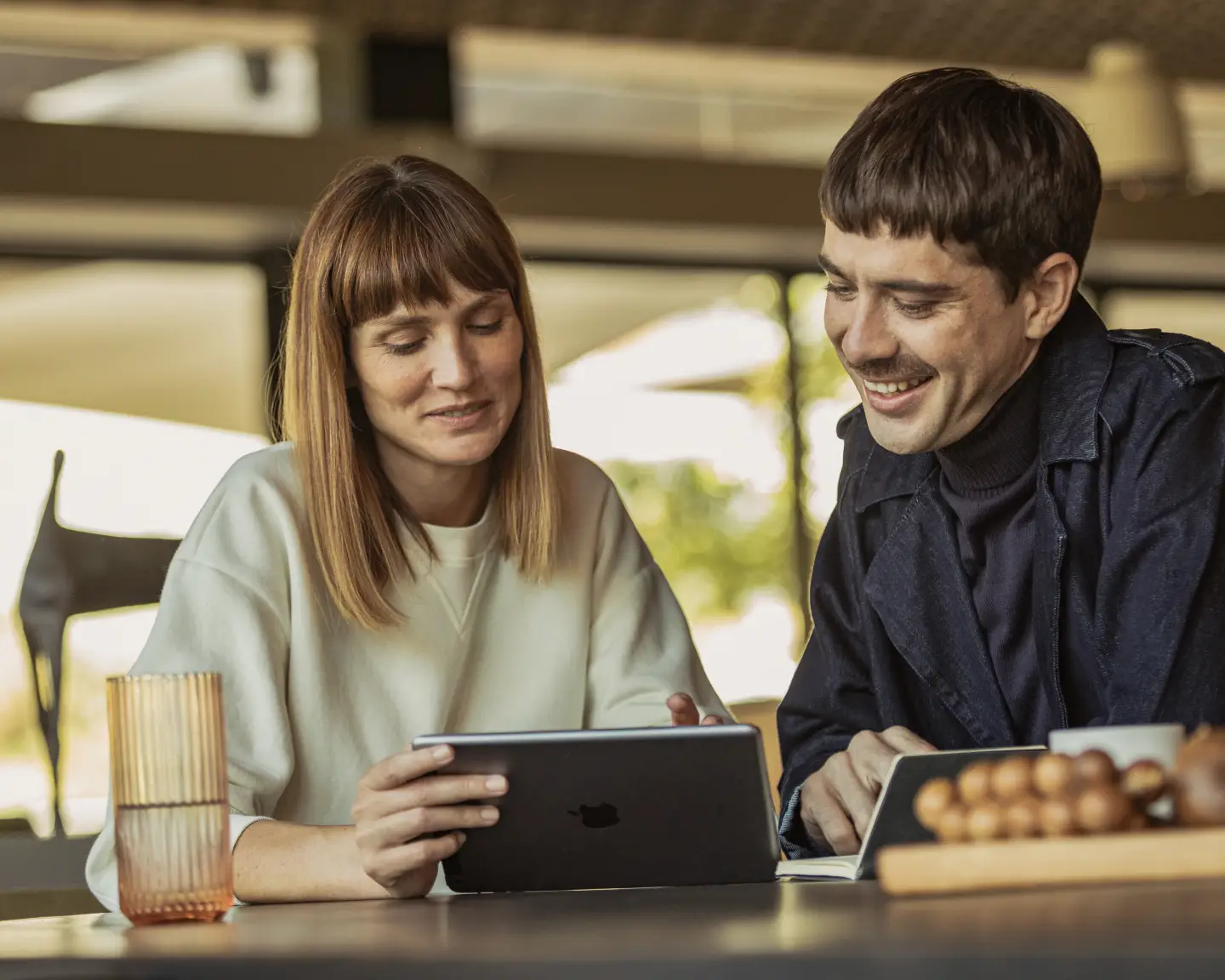 Een jonge man en een jonge vrouw zitten aan een tafel en kijken naar hun tablet.