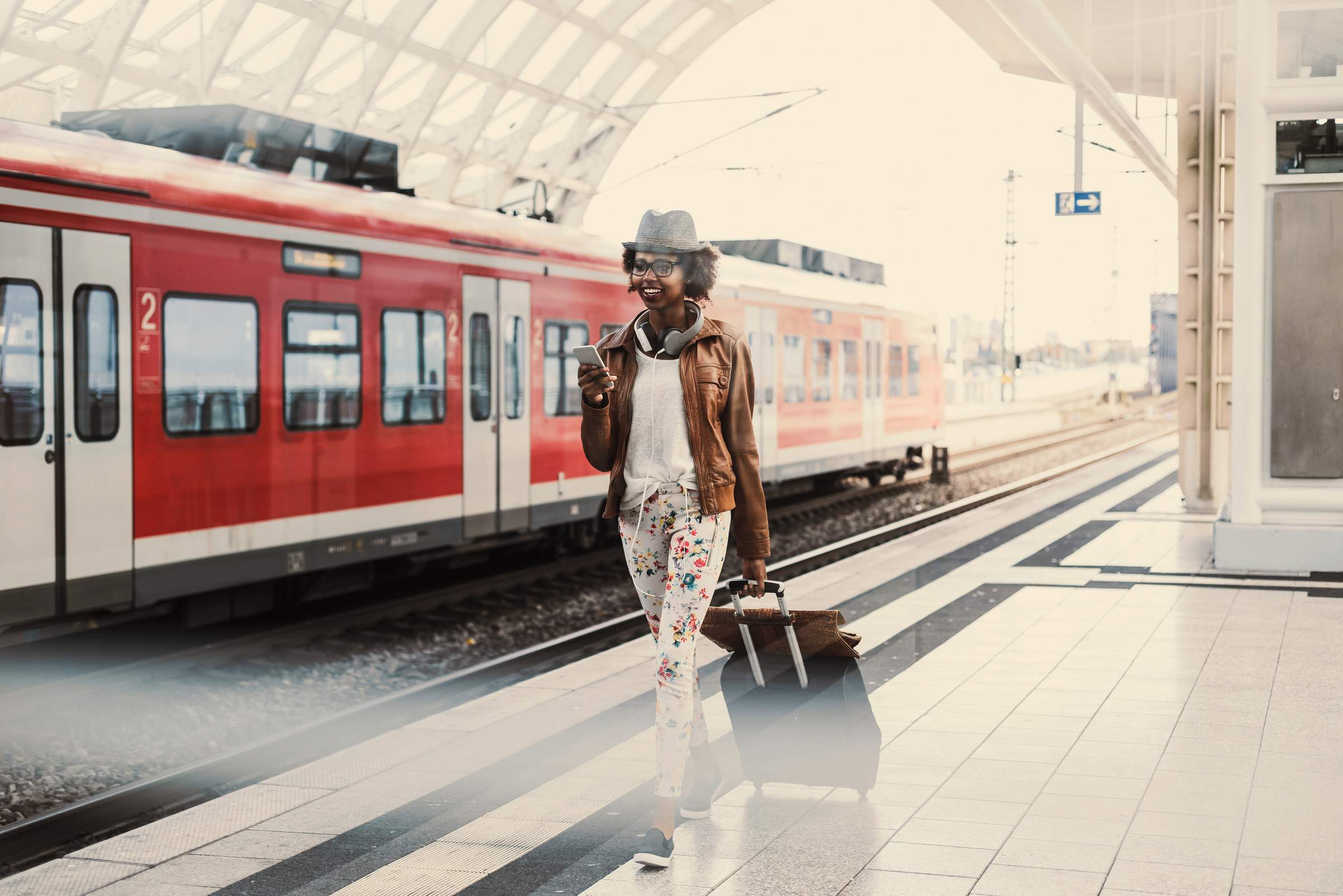 Eine Frau läuft mit einem Koffer am Bahnsteig entlang, im Hintergrund ein roter Zug der deutschen Bahn.